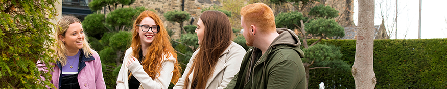 4 students sat on a bench at Creative campus gardens chatting and smiling